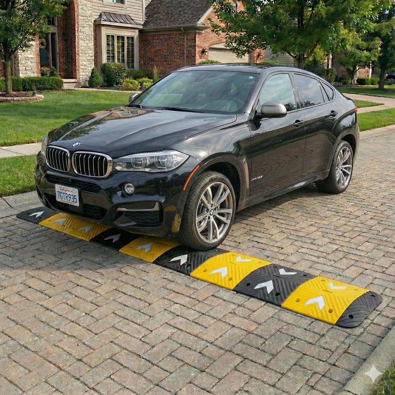 Yellow and black rubber speed bump bolted across a luxury residential driveway with a BMW X6 crossing it
